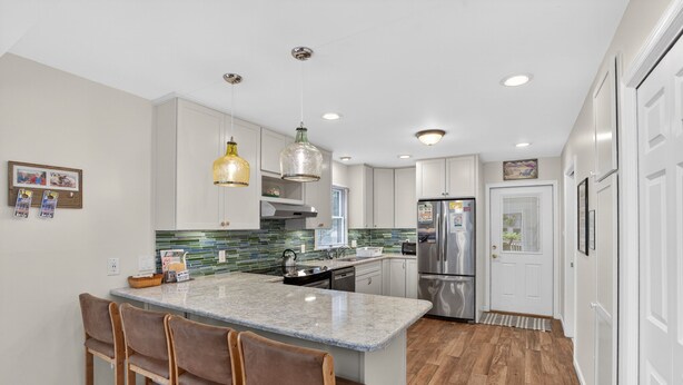 A modern kitchen with a marble island, bar stools, pendant lighting, and stainless steel appliances.