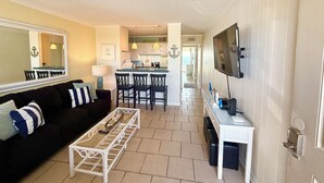 A living room with a sofa, coffee table, TV, and a kitchen area with bar stools. - Third Floor Private Beach Terrace (Fort Walton Beach)