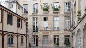 Un cortile con pavimentazione in pietra, un edificio con numerose finestre e balconi, e un po' di verde sui balconi.