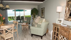 Una sala de estar con vista al océano, un comedor con sillas y una mesa, y un mueble de madera con un marco de fotos.