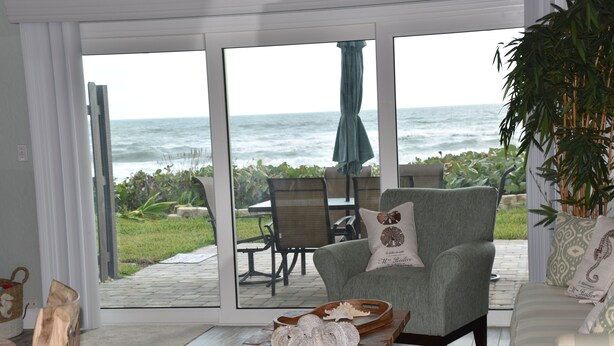 Una habitación con vista al océano, un sillón verde, una mesa de centro de madera con objetos decorativos y un sofá con cojines estampados.