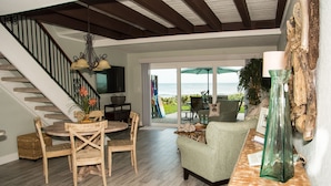 Amplia sala de estar con mesa de comedor de madera, sillas, un sofá y un ventanal con vistas al exterior.