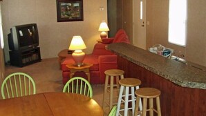 Un espace de vie compact comprenant une table à manger, des tabourets de bar, un téléviseur et un tableau accroché au mur.