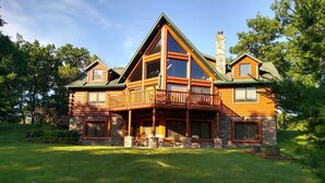 A log cabin with a stone foundation, a balcony, and a chimney.