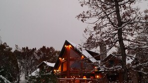 A log cabin with a balcony, surrounded by snow-covered trees.