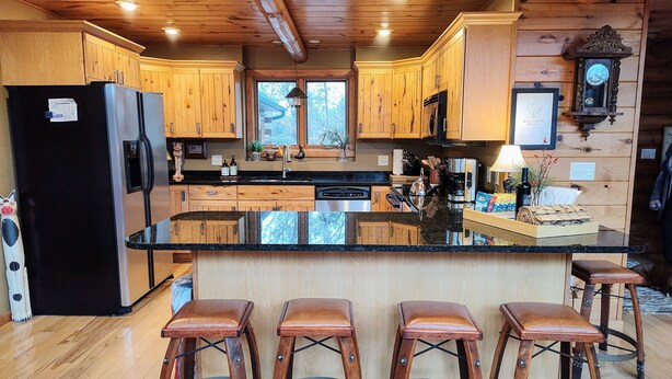 A kitchen with wooden cabinets, a black refrigerator, a large island with stools, and a clock on the wall.