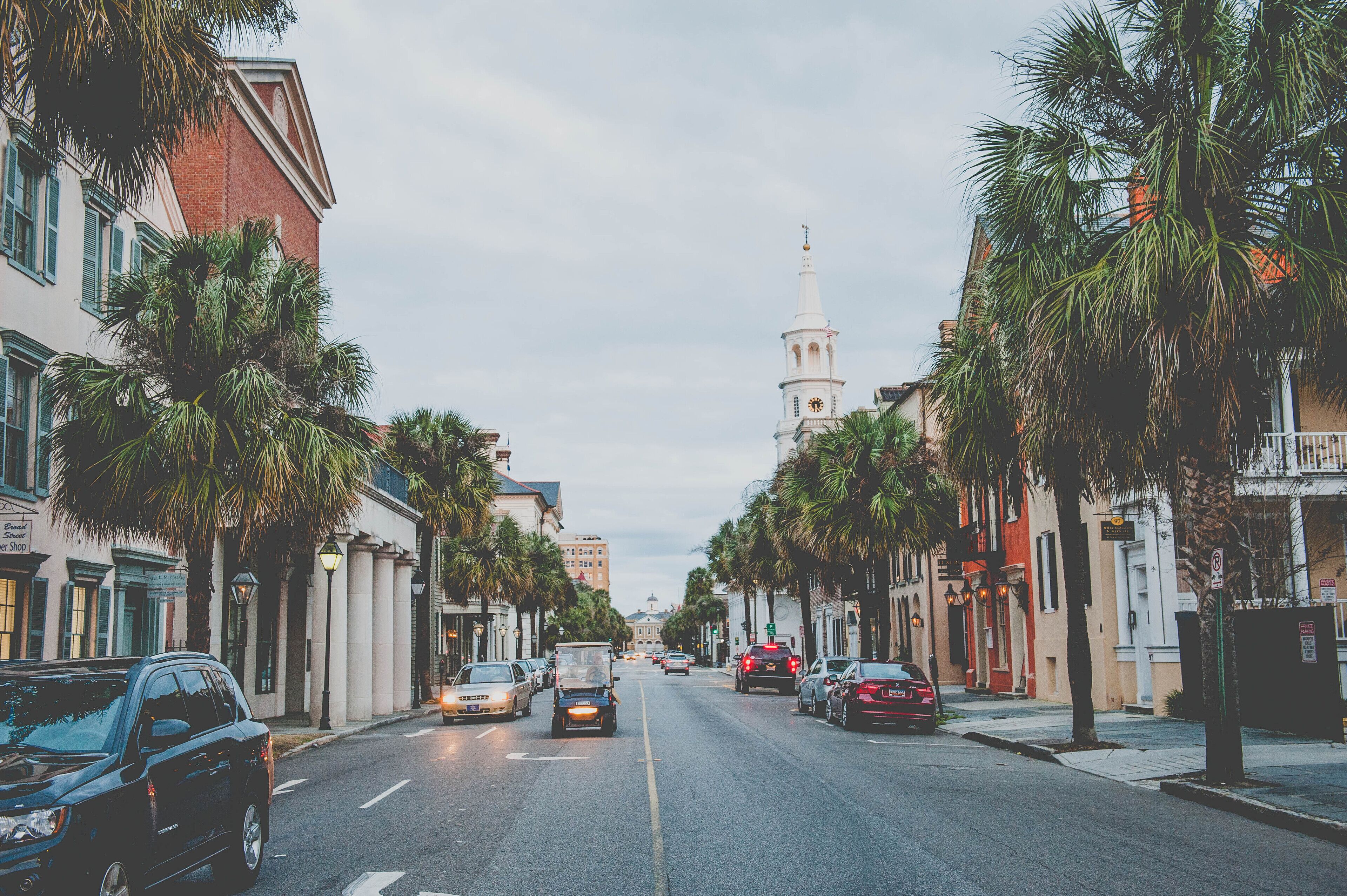 A street lined with palm trees and historic buildings, including a church with a tall steeple.