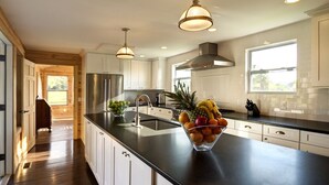 A modern kitchen with white cabinets, a black countertop, and a fruit bowl.