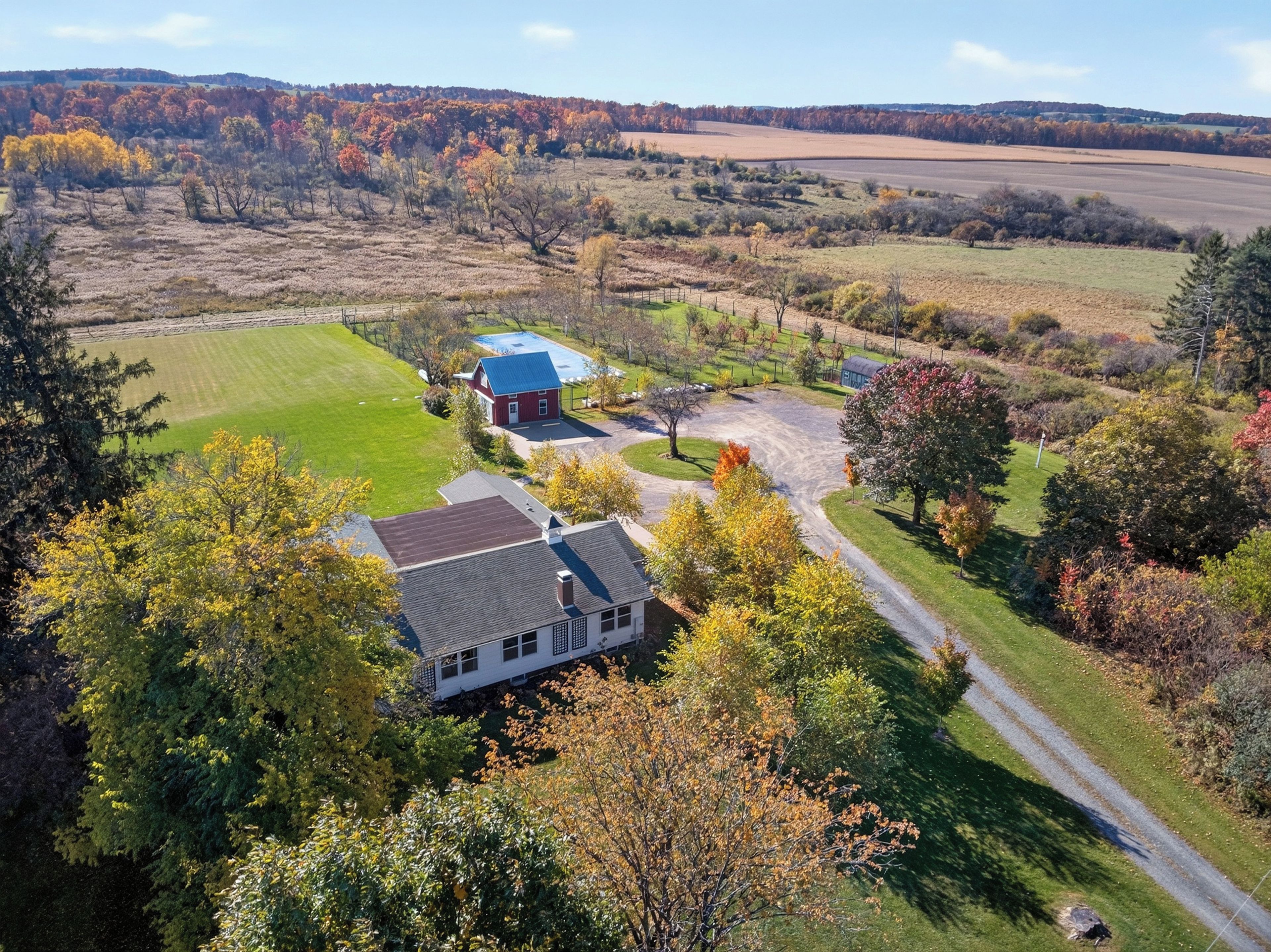 Uma propriedade rural com uma casa grande, um prédio menor vermelho e um gramado bem cuidado.