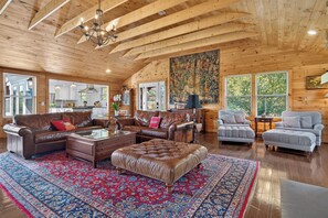 A spacious living room with a high ceiling, wooden beams, and a large window.