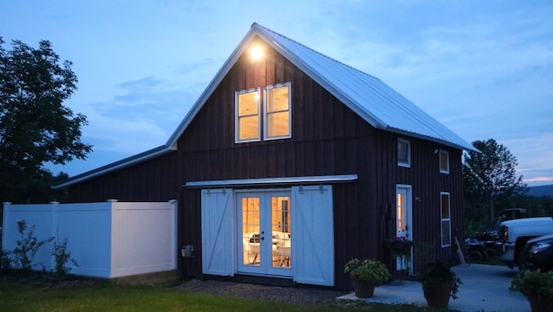 A large, dark wooden barn with a gabled roof and a sliding door entrance.