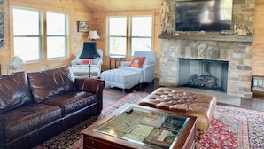 A cozy living room with a stone fireplace, leather sofas, and a television mounted above it.
