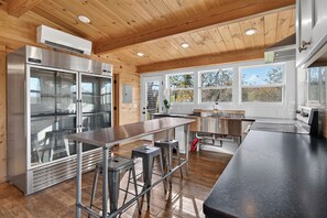 A modern kitchen with stainless steel appliances, wooden ceiling, and large windows.