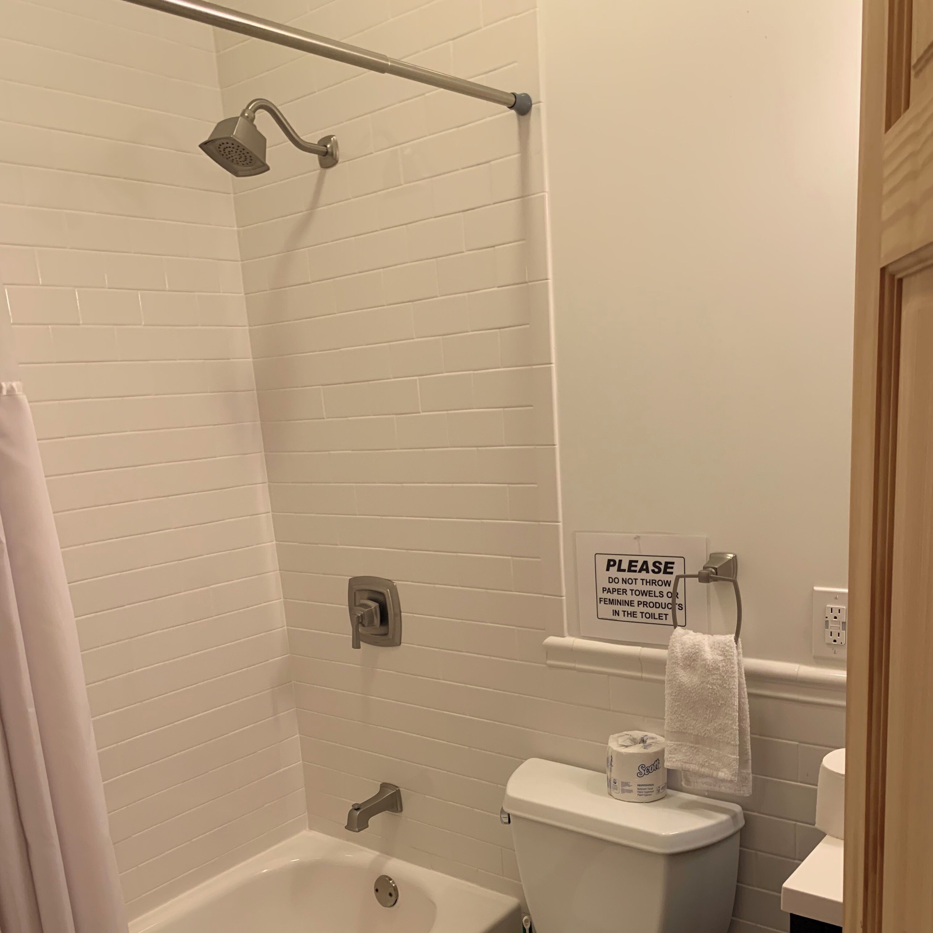 A bathroom with a shower, toilet, and bathtub. There is a sign on the wall advising not to throw paper towels or feminine products in the toilet.