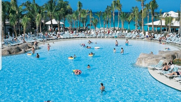 Une grande piscine extérieure dotée de plusieurs couloirs, entourée de palmiers et de chaises longues.