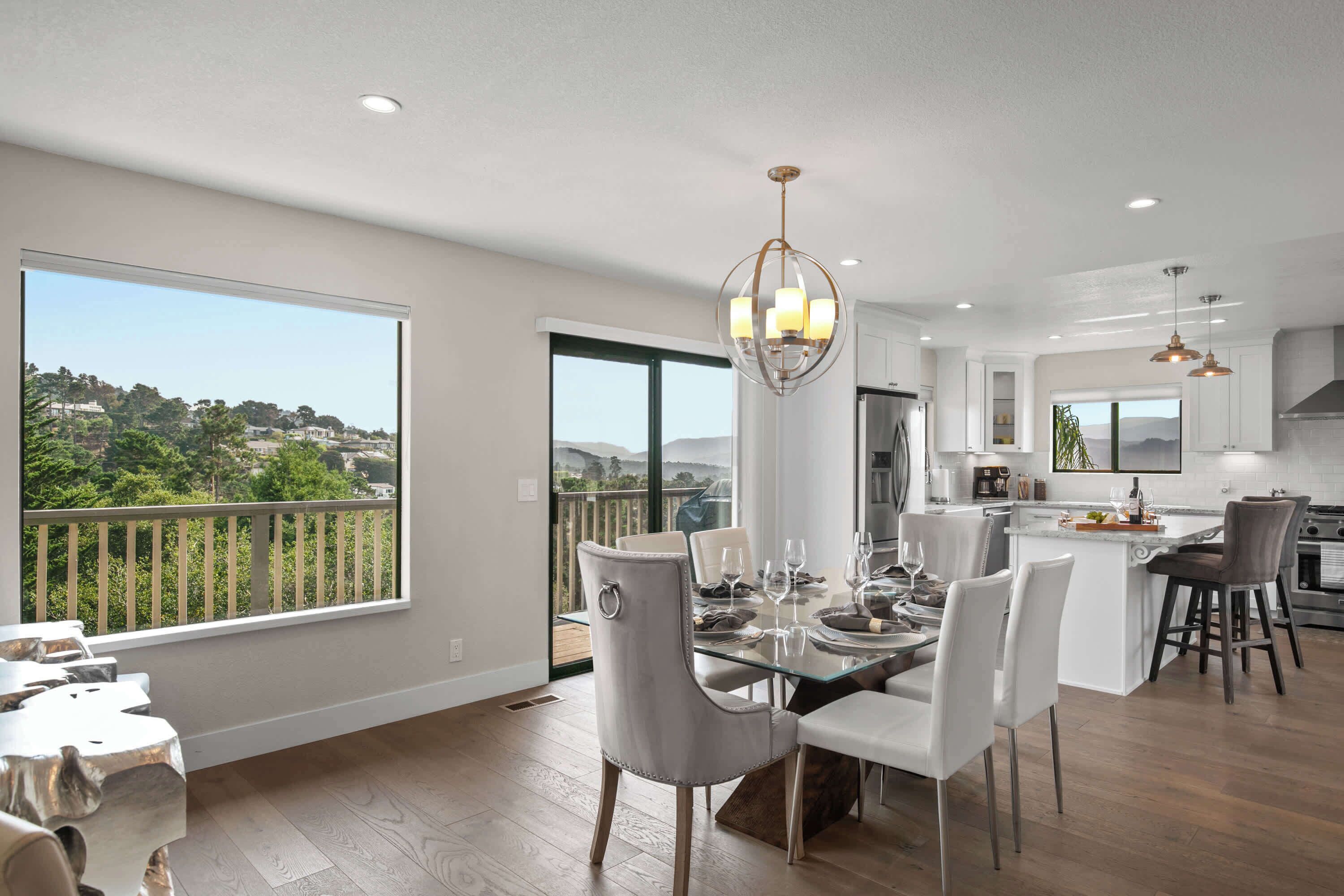 A modern kitchen with a dining area, large windows, and a view of a residential area.