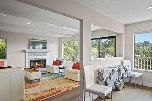 A spacious living room with a fireplace, comfortable seating, and large windows offering a view of the outdoors.