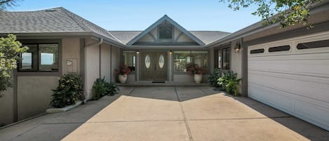 A two-story house with a garage, a front porch with potted plants, and a driveway.