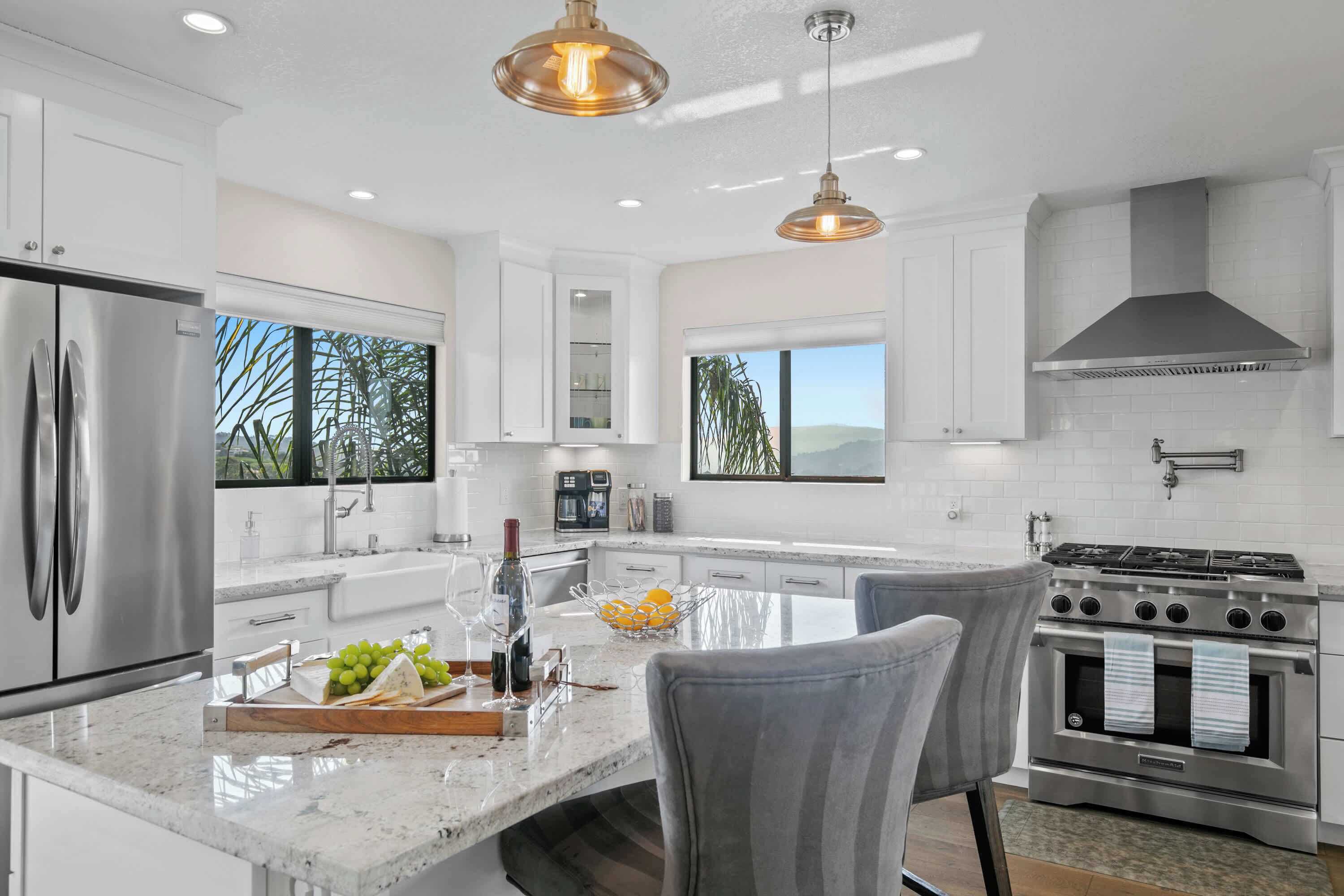 A modern kitchen with white cabinetry, a stainless steel refrigerator, a built-in oven, and a large island with seating.