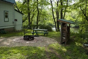 Een rustieke buitenruimte met een picknicktafel, een vuurkuil en een klein houten prieeltje.