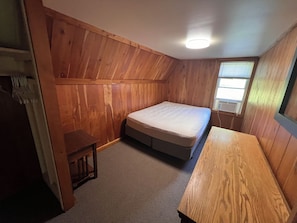 Een slaapkamer met een houten plafond, een enkel bed, een tafeltje en een raam met jaloezieën.