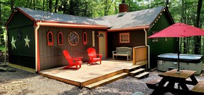 Uma cabana com varanda, duas cadeiras Adirondack vermelhas, um banco, hidromassagem e uma mesa de piquenique.