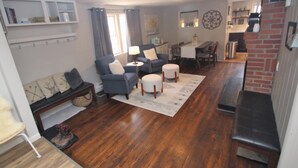 Ein Wohnzimmer mit einer Sofagarnitur, einem Couchtisch und einem Teppich. Es gibt einen Essbereich mit Tisch und Stühlen.