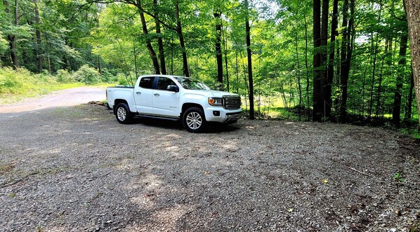 Una camioneta pickup blanca aparcada sobre un camino de grava rodeada de un denso bosque verde.