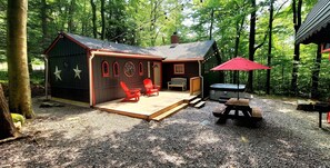 Una cabaña con terraza, sillas rojas, una mesa y un paraguas rojo.