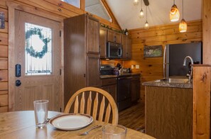 A wooden cabin interior with a dining table, chairs, a refrigerator, a microwave, and a sink.