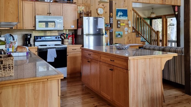 A rustic kitchen with wooden cabinets, a large island, and a staircase leading to an upper level.