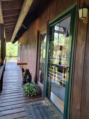 A wooden porch with a welcome sign, a bird sculpture, and a flower arrangement.