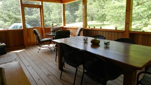 A wooden deck with a dining table and chairs, large windows, and a ceiling fan.