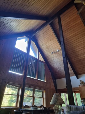 A high-ceilinged room with wooden beams, large windows, and a dining area with chairs and a table.