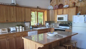 A kitchen with wooden cabinets, a central island with stools, a microwave, and a refrigerator.
