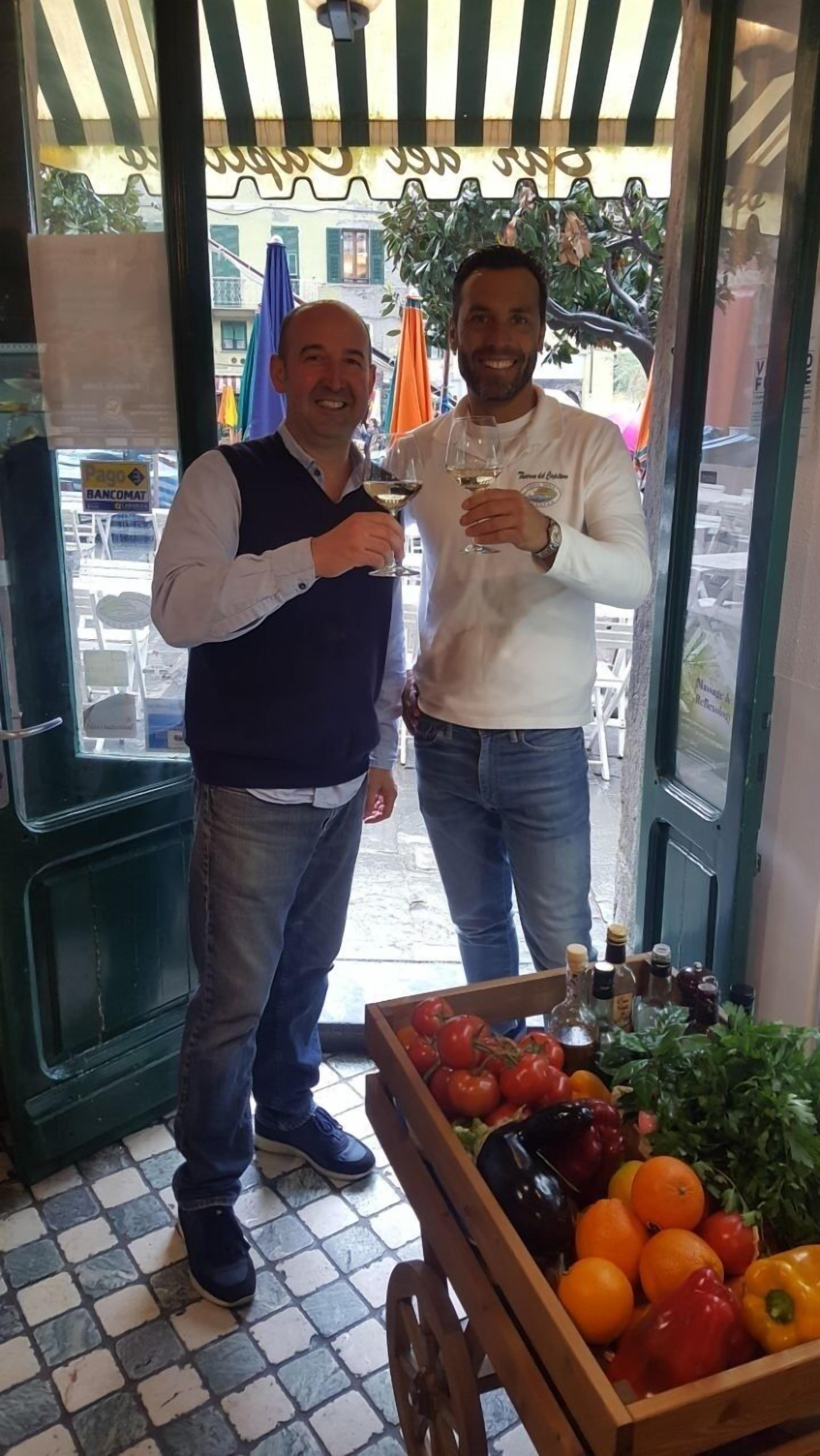 Zwei Männer stehen in einem Laden, in dem frisches Obst und Gemüse sowie Flaschen ausgestellt sind.