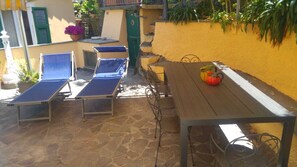 Une terrasse avec des chaises longues et une table en bois, entourée d’un mur jaune et de plantes en pot.