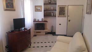 Ein Wohnzimmer mit Fernseher auf einer Holzkommode, einer Couch, einem Kamin und Regalen mit Dekoration.