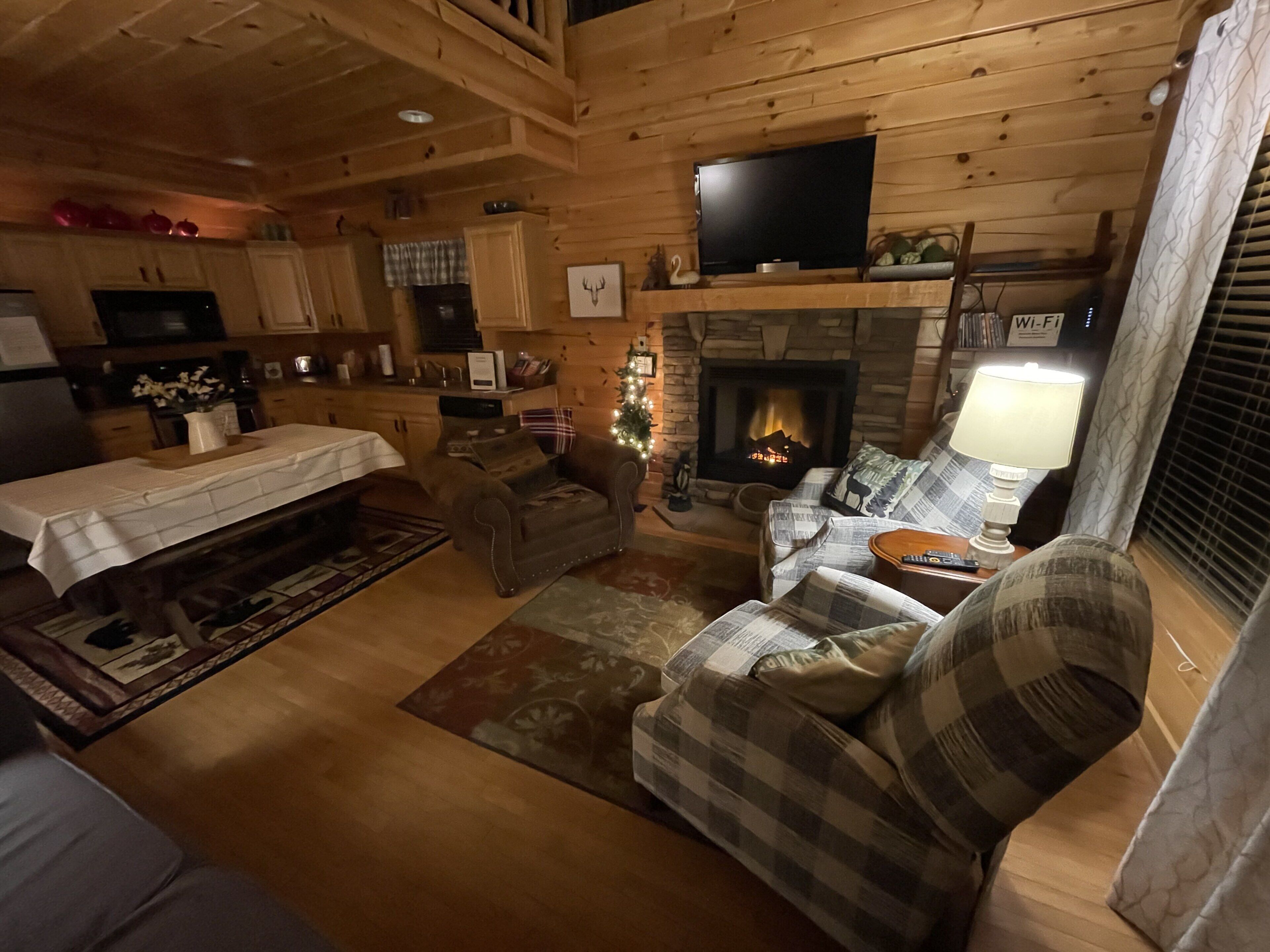 Interior acollidor d'una cabana amb una llar de foc, parets de fusta, una televisió i zona de menjador.