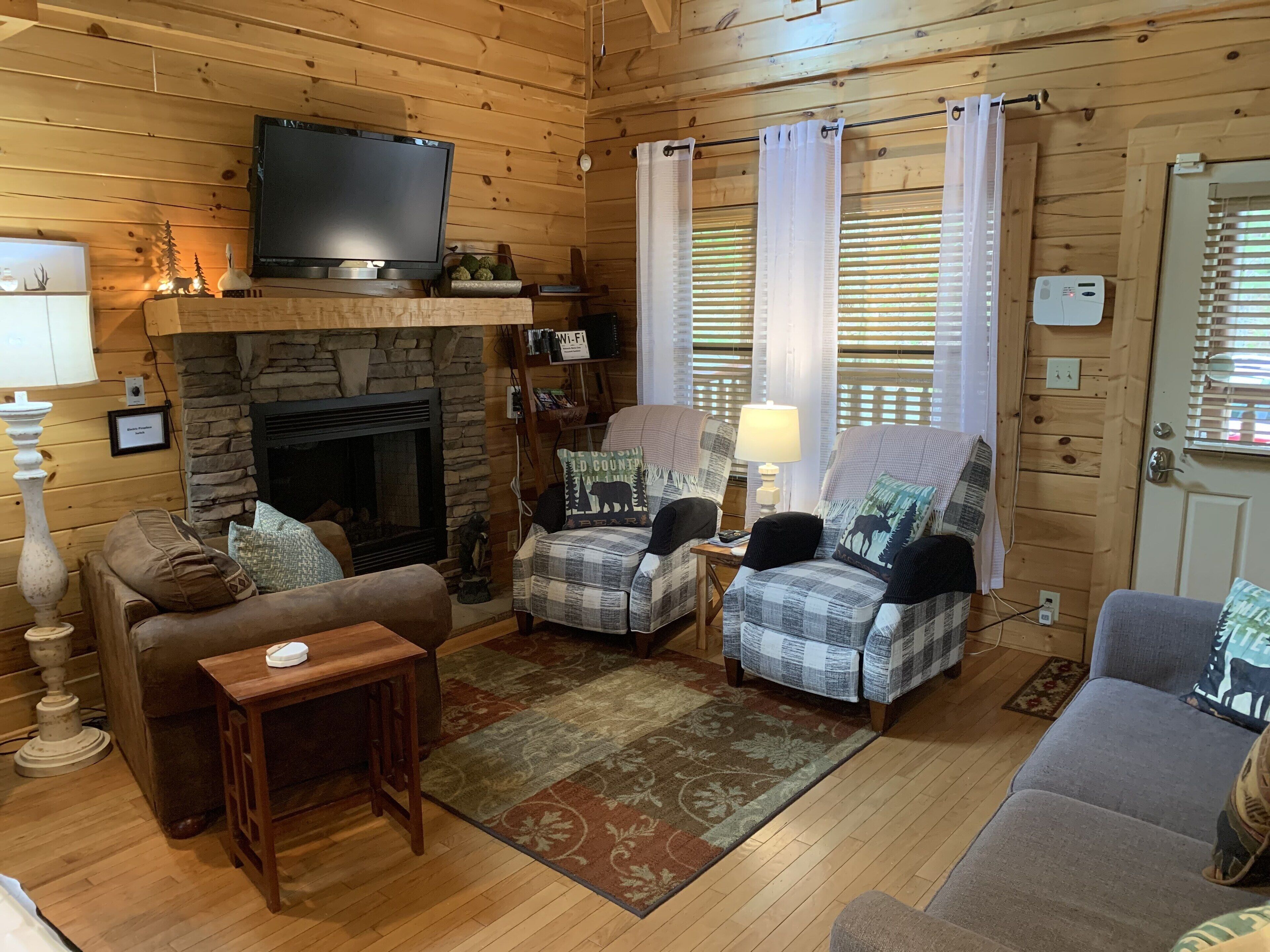 A cozy cabin interior with a stone fireplace, wooden walls, a television, and comfortable seating.