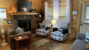A cozy cabin interior with a stone fireplace, wooden walls, a television, and comfortable seating.