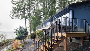 A modern house with a wooden deck and a staircase leading to a balcony. - Stunning Waterfront - PNW Gem,  Hot Tub, Mountain Views, Fireplace (Olympia)