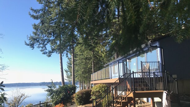 A cabin with a deck and stairs leading to a balcony overlooking a lake. - Stunning Waterfront - PNW Gem,  Hot Tub, Mountain Views, Fireplace (Olympia)