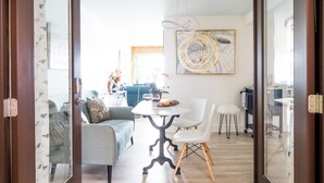 A modern living room with a dining area, featuring a round table, white chairs, and a large abstract painting on the wall. - Stunning Waterfront - PNW Gem,  Hot Tub, Mountain Views, Fireplace (Olympia)