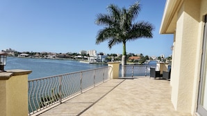 A balcony with a view of a body of water, a palm tree, and a building with a tiled floor. - Waterfront Paradise in Marco Island (Marco Island)