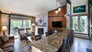 A spacious living area with a fireplace, a large TV mounted on the wall, and a dining area with a long island counter. - 2 BR Updated Condo-Mountain View! Excellent location, views & value! (Breckenridge)