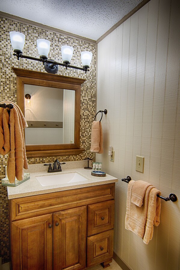 A bathroom with a wooden vanity, a large mirror, and three wall-mounted lights.