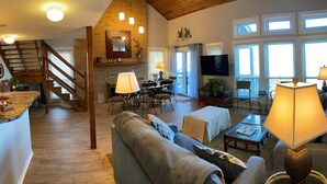 A spacious living area with a wooden staircase, a dining set, and a sofa with a lamp.