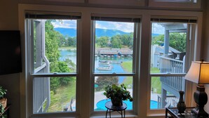 A room with multiple windows overlooking a lake, a pool, and a dock area.