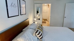 A neatly made bed with white linens and a striped pillow, a bedside table with a lamp, and two framed signs on the wall. - 360A - Boca Retreat w/ Pool, Parking, Near Evert Tennis & Shops (Boca Raton)